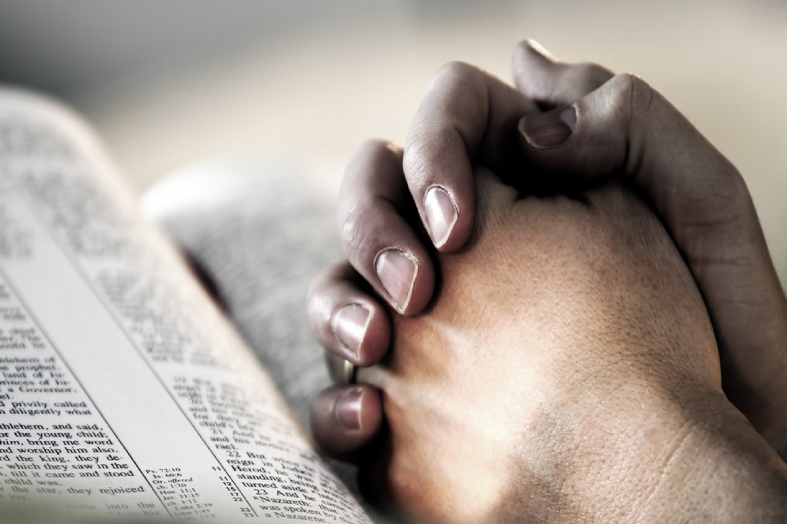 Man's hands folded in prayer over a Holy Bible - represents faith and spirtuality in everyday life.